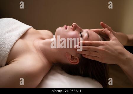 Terapista femminile massaggiando il viso e la fronte di un cliente rilassato a una giovane donna. Massaggio rilassante. Massaggio viso. Medicina alternativa. Foto Stock