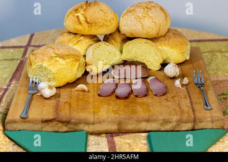 Primo piano di alimenti biologici. Affumicato di carne al tavolo con aglio e pane fatto in casa su un asse di legno. Foto Stock