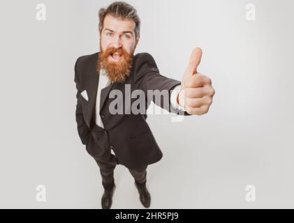 Emozionato uomo d'affari stupito in vestito nero sorridente e mostrando pollici in su. Fuga dalla crisi. Faccia divertente. Ottima idea. Ritratto di uomo eccitato gesturing Foto Stock