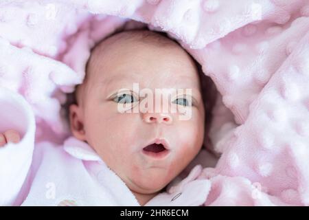 Ritratto di una bambina appena nata che apre la bocca che giace nella sua culla su una morbida coperta rosa Foto Stock
