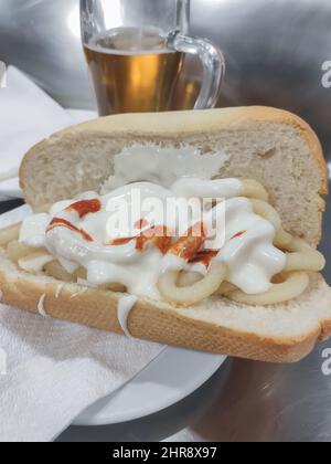 Sandwich al calamari con birra in background. Tipico cibo spagnolo, bocadillo de calamares di Madrid. Foto Stock