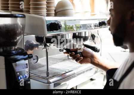 Barista afroamericano che utilizza la macchina per il caffè mentre prepara la bevanda acafe Foto Stock