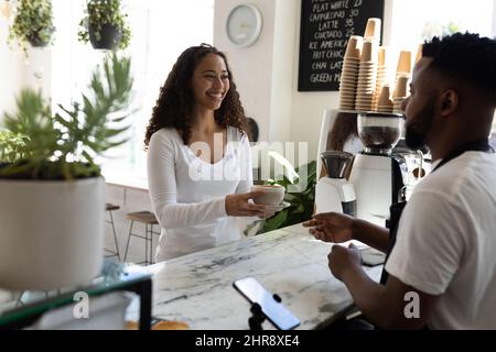 Sorridendo il giovane cliente afro-americano che ha preso la tazza di caffè dal barista al banco del caffè Foto Stock