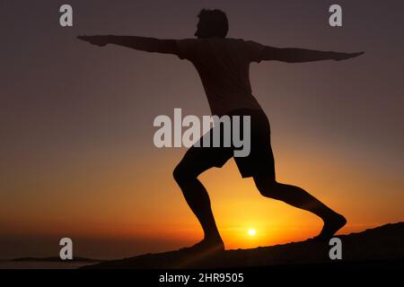 Stretching nella luce in diminuzione. Silhouette di un uomo che fa esercizi con il tramonto sullo sfondo. Foto Stock