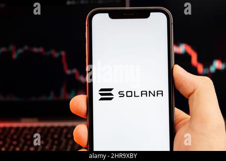 Solana Sol logo criptovaluta sullo schermo di smartphone in mano mans con tendenza al ribasso sulla carta su sfondo rosso, febbraio 2022, San Francisco, USA. Foto Stock