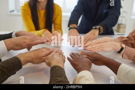 Un team diversificato di uomini d'affari che si uniscono alle loro mani durante una riunione intorno a un tavolo d'ufficio Foto Stock