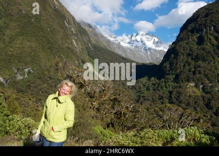 Donna sorridente in piedi di fronte al paesaggio di montagna, Milford, South Island, Nuova Zelanda Foto Stock