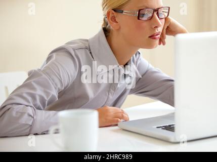 Troppo stanco e sottopagato. Una giovane donna d'affari annoiato e stanca che sta fissando lo schermo del suo laptop. Foto Stock