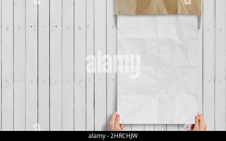 La mano tirando la carta stropicciata da riciclare busta bianca su sfondo legno Foto Stock