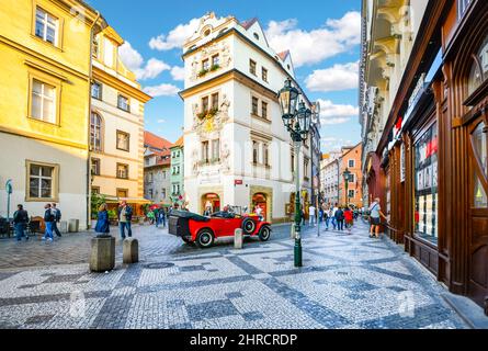 I turisti passeggiata, shop e gustare il caffè come essi passano da un rosso vintage automobile in una sezione di pittoresca della Città Vecchia di Praga, Repubblica Ceca. Foto Stock