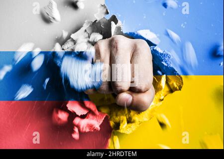 Un pugno attraversa un muro di cemento con i colori delle bandiere ucraine e russe. Il concetto di aggressione russa contro l'Ucraina Foto Stock
