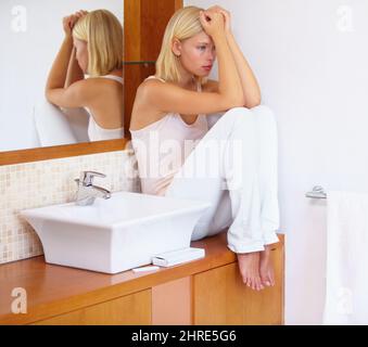 Non posso avere un bambino ora. Una giovane donna seduta sul bancone del bagno accanto a un test di gravidanza mentre guarda disprezzare. Foto Stock