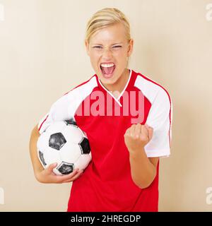 Campioni del campionato. Scatto di una giovane donna vestita in una divisa da calcio che celebra e tiene in mano una palla da calcio. Foto Stock