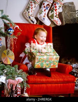 1970S 1980S FELICE RIDENDO LA BAMBINA TODDLER SEDUTA NELLA SEDIA GRANDE ROSSA VIVENTE DELLA STANZA DALL'ALBERO DI NATALE CHE DISINCARTANO UN REGALO PRESENTE - KX9470 PHT001 HARS RIDERE INFANTE DECORAZIONI FELICE GIOIA LIFESTYLE SODDISFAZIONE FESTEGGIAMENTI FEMMINE HOME VITA COPIA SPAZIO FELICITÀ MEZZA LUNGHEZZA ALLEGRO SCOPERTA SOGGIORNO STANZA ALLEGRO ECCITAZIONE VICINO IN VACANZE SORRISI DICEMBRE 25 GIOIOSA DISIMBALLAGGIO GIOVANI GIOVANI RAGAZZA CAUCASICA BAMBINO ETNIA VECCHIO STILE Foto Stock