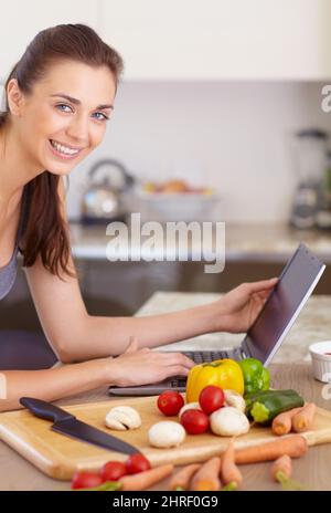 Controllare Internet per una buona ricetta. Ritratto di una bella giovane donna alla ricerca di ricette sul suo tablet digitale durante la cottura. Foto Stock