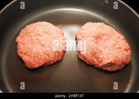 Friggere gli hamburger in una padella nera Foto Stock