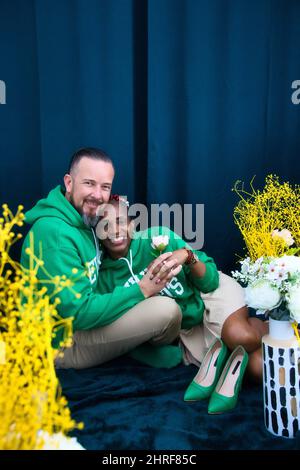 Foto studio verticale della felice coppia multirazziale nelle stesse felpe verdi che si posano insieme Foto Stock