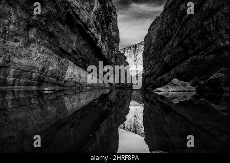 Un'immagine drammatica in scala di grigi di una profonda gola con formazione rocciosa riflessa nell'acqua Foto Stock