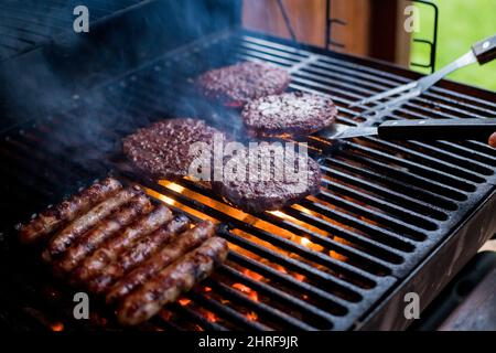 Hamburger affumicati grigliate di carne per hamburger. Friggete sul fuoco aperto sulla griglia - bbq.Burgers e salsicce che cuocono su Flames sul Grill. Foto Stock