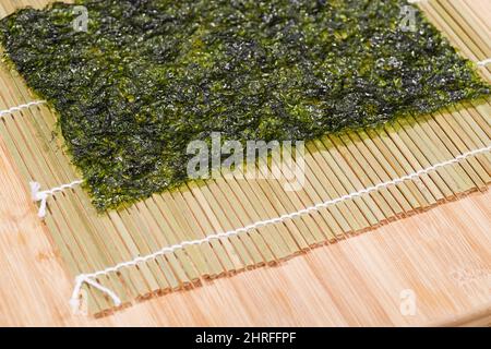 Sushi ingredienti, nori alghe makisu sul tappetino di bambù per  laminazione, crudo fresco salmone, materie di riso sushi, la salsa di soia  e bacchette sul lato Foto stock - Alamy