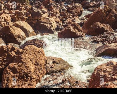 Il flusso di fiume di montagna bolle tra le pietre rosse nella gola della campagna caucasica nell'illuminazione del sole autunnale Foto Stock