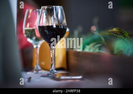 Camera romantica con bicchieri da vino in interni di lusso. Due bicchieri di vino con vino rosso e bianco sono sul tavolo in camera con fiori. Spazio di copia Foto Stock