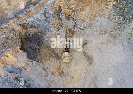 L'escavatore carica la roccia estratta nel dumper per la macchina frantumatrice per pietre durante i lavori di movimento terra Foto Stock