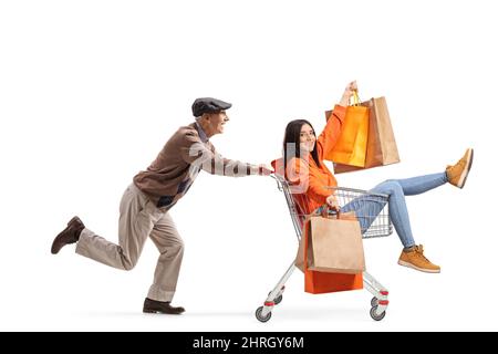 Uomo anziano che spinge una giovane femmina all'interno di un carrello con borse shopping isolato su sfondo bianco Foto Stock