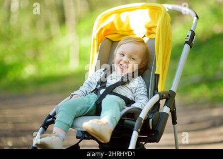 Dolce ragazzo bambino seduto in un passeggino all'aperto. Bambino piccolo in pram. Bambino in passeggino. Passeggiate estive con bambini. Divertimento in famiglia con Little ch Foto Stock