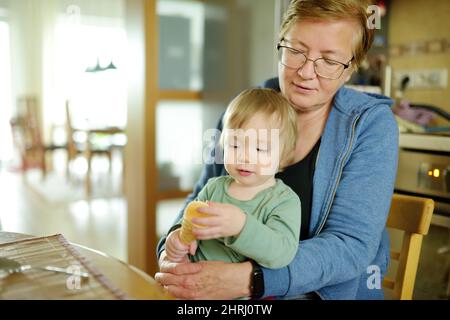 Nonna che tiene il suo nipote del toddler in una cucina. Nonna coccola con il nipote. Trasporto di un bambino. Foto Stock