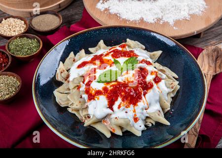 Ravioli turchi perfetti e peperoncini fritti nel burro. Manti manlama Turca su piatto con pepe rosso, salsa di pomodori, yogurt e menta. Piastra da Foto Stock