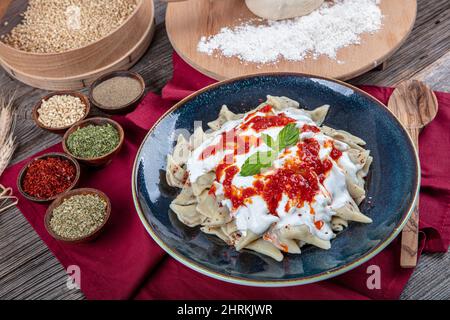 Ravioli turchi perfetti e peperoncini fritti nel burro. Manti manlama Turca su piatto con pepe rosso, salsa di pomodori, yogurt e menta. Piastra da Foto Stock