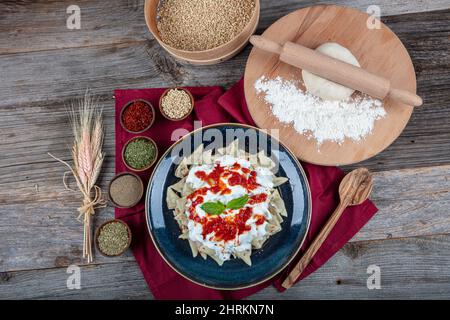 Ravioli turchi perfetti e peperoncini fritti nel burro. Manti manlama Turca su piatto con pepe rosso, salsa di pomodori, yogurt e menta. Piastra da Foto Stock