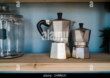 Due vecchi bollitori da caffè in metallo posti su un ripiano di legno e pareti blu chiaro sullo sfondo Foto Stock