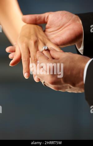 Fare un voto. Vista spezzata di uno sposo che scivola un anello sul suo dito sposa. Foto Stock