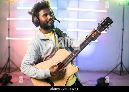 Giovane artista musicale professionista che suona la chitarra cantando sul palco con sfondo neon ligt - concetto di musicista, intrattenimento e passione Foto Stock