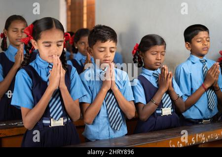 Studenti in classe che fanno la preghiera mattutina con occhi chiusi - concetto di saggezza, amicizia, sviluppo e disciplina. Foto Stock