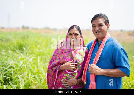 Ritratto girato di sorridente coppia di villaggio indiano al prato guardando la macchina fotografica - concetto di famiglia felice, stile di vita rurale e la convivenza Foto Stock