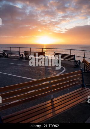 Alba arancione dorata su una linea di panchine deserte a Teignmouth nel Devon. I posti a sedere vuoti si affacciano sul mare senza nessuno in vista. Copy space.calm Foto Stock