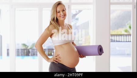 Stare in forma per il mio bambino. Ritratto corto di una giovane donna incinta attraente che porta un tappeto yoga. Foto Stock