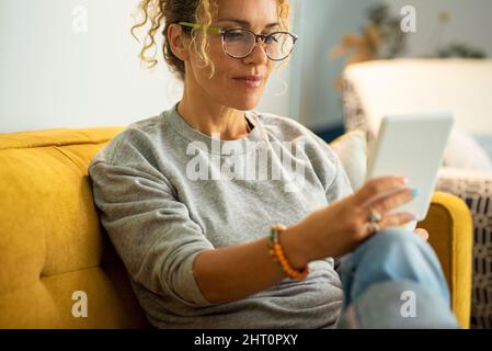 Primo piano tratto di donna moderna adulti persone leggere libro da lettore elettronico tablet dispositivo. Signora indossare occhiali e sorridere godendo di rel Foto Stock