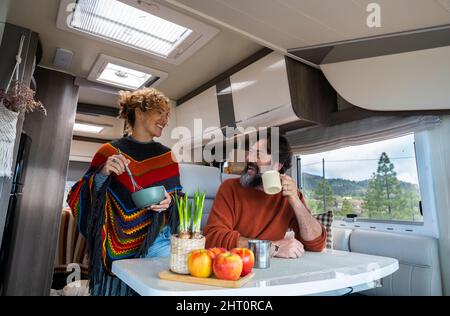 Coppia caucasica di vanlifers o turista godere di attività di tempo libero di cottura all'interno del camper con incredibile vista libera della natura fuori dalla finestra. Felice m Foto Stock