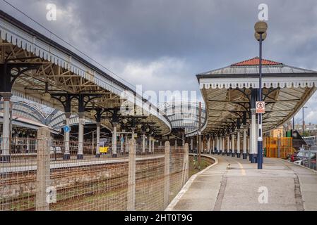 Un sentiero in pendenza conduce fino ad una storica stazione ferroviaria con un baldacchino ad arco sullo sfondo. Un cielo con le nuvole scure è sopra. Foto Stock