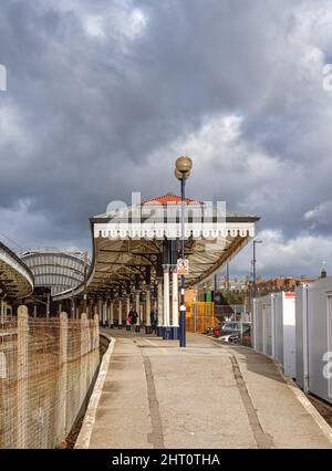 Un sentiero in pendenza conduce fino ad una storica stazione ferroviaria con un baldacchino ad arco sullo sfondo. Un cielo con le nuvole scure è sopra. Foto Stock