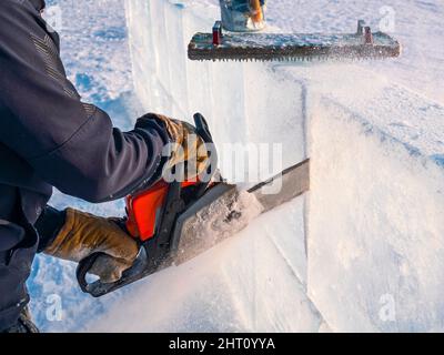 Realizzare sculture di ghiaccio. Un uomo taglia la superficie in un blocco di ghiaccio con una sega a benzina sul lago Baikal. Foto Stock