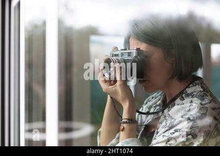 Donna adulta che fotografa con la macchina fotografica dalla finestra della sua casa. Spazio per il testo. Foto Stock