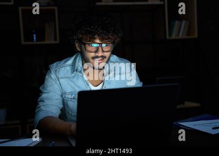 Giovane uomo indiano che lavora a tarda notte con un computer portatile. Foto Stock