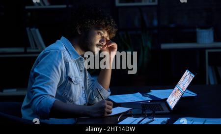 Uomo d'affari indiano concentrato che ha videochiamata riunione virtuale a tarda notte. Foto Stock