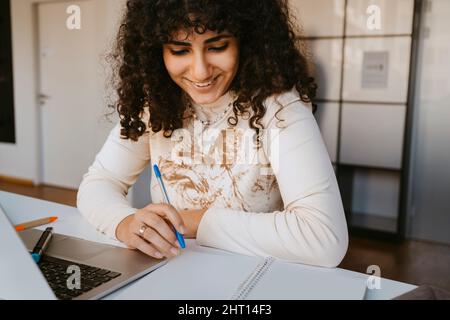 Giovane donna sorridente con capelli ricci che studia all'università della comunità Foto Stock