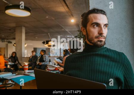 Uomo giovane e premuroso seduto con un computer portatile nella caffetteria dell'università Foto Stock